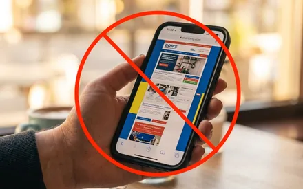 A hand holding a phone showing a cluttered, hard-to-use plumbing website, marked with a red no-entry symbol